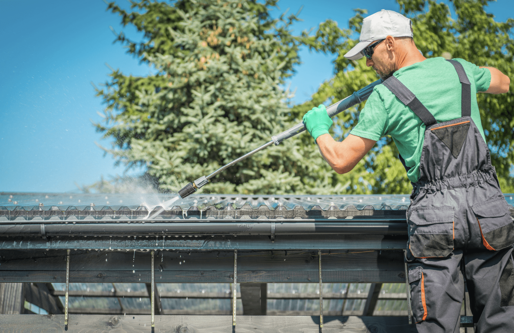 A man in green overalls cleaning out gutters with a pressure hose