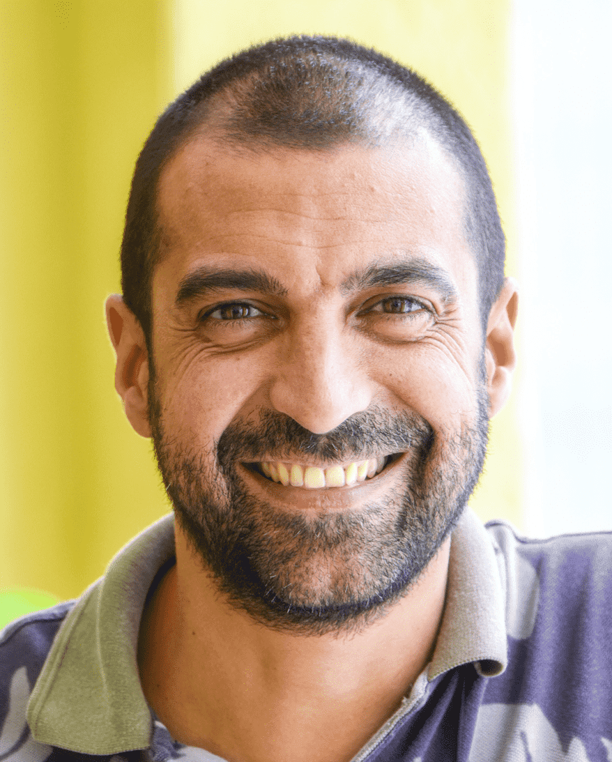 A headshot of a middle-aged man with peppered hair wearing a purple t-shirt